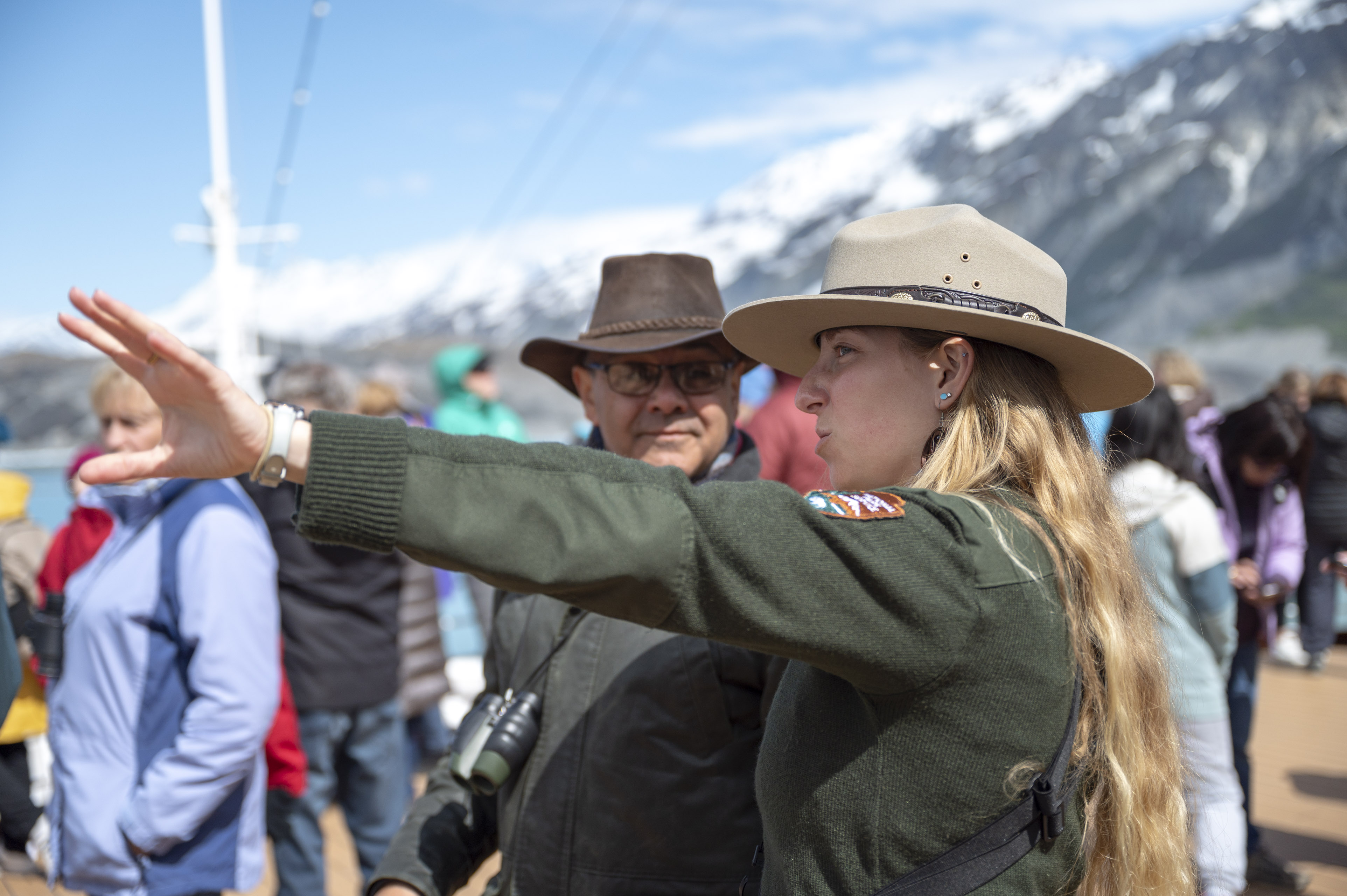 Ranger with visitor Park Ranger points with an open hand off-screen while a visitors listens.