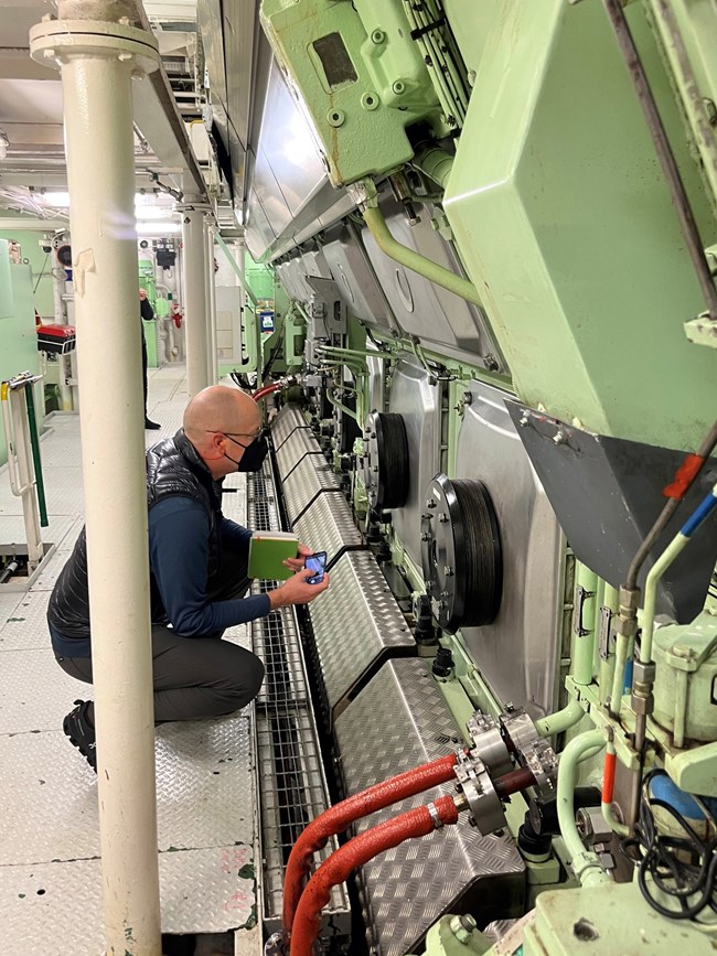 Cruise Ship Inspection Inspector looking at cruise ship engine components in a brightly lit engine room.