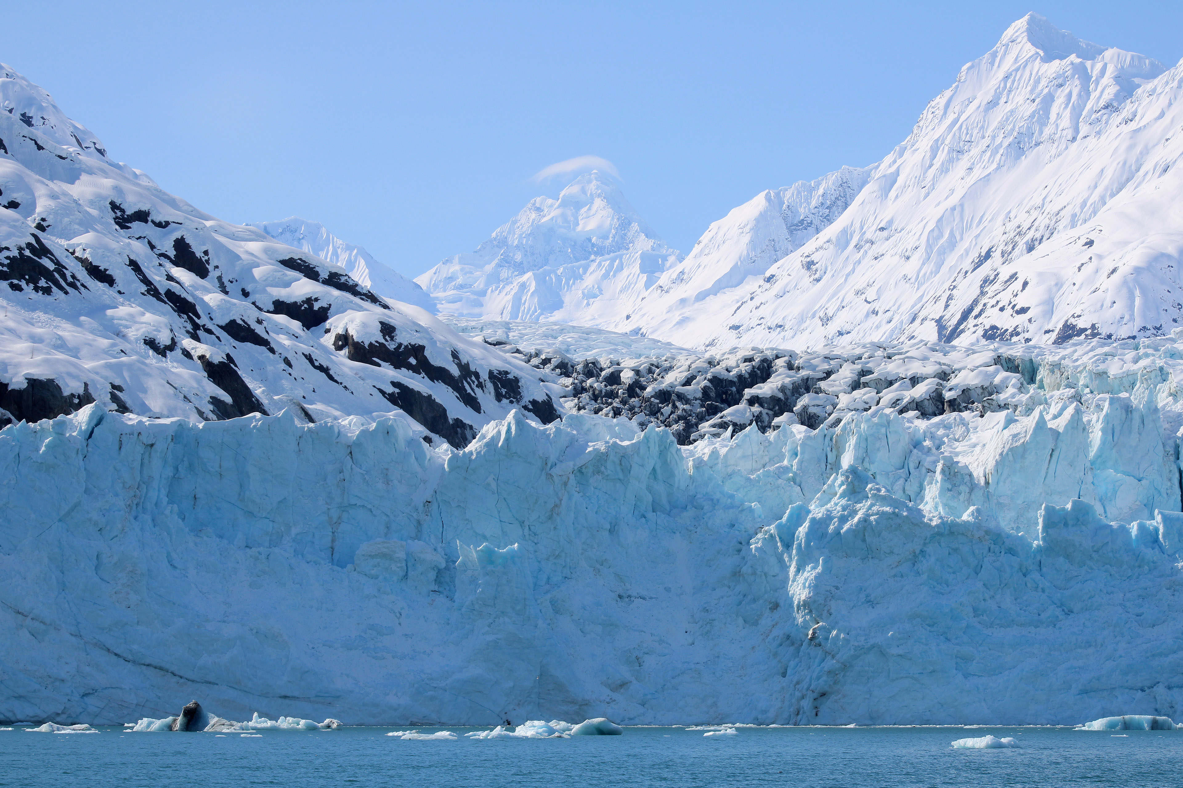 Bright blue ice is covered in white snow with snowcapped mountains surrounding the scene.