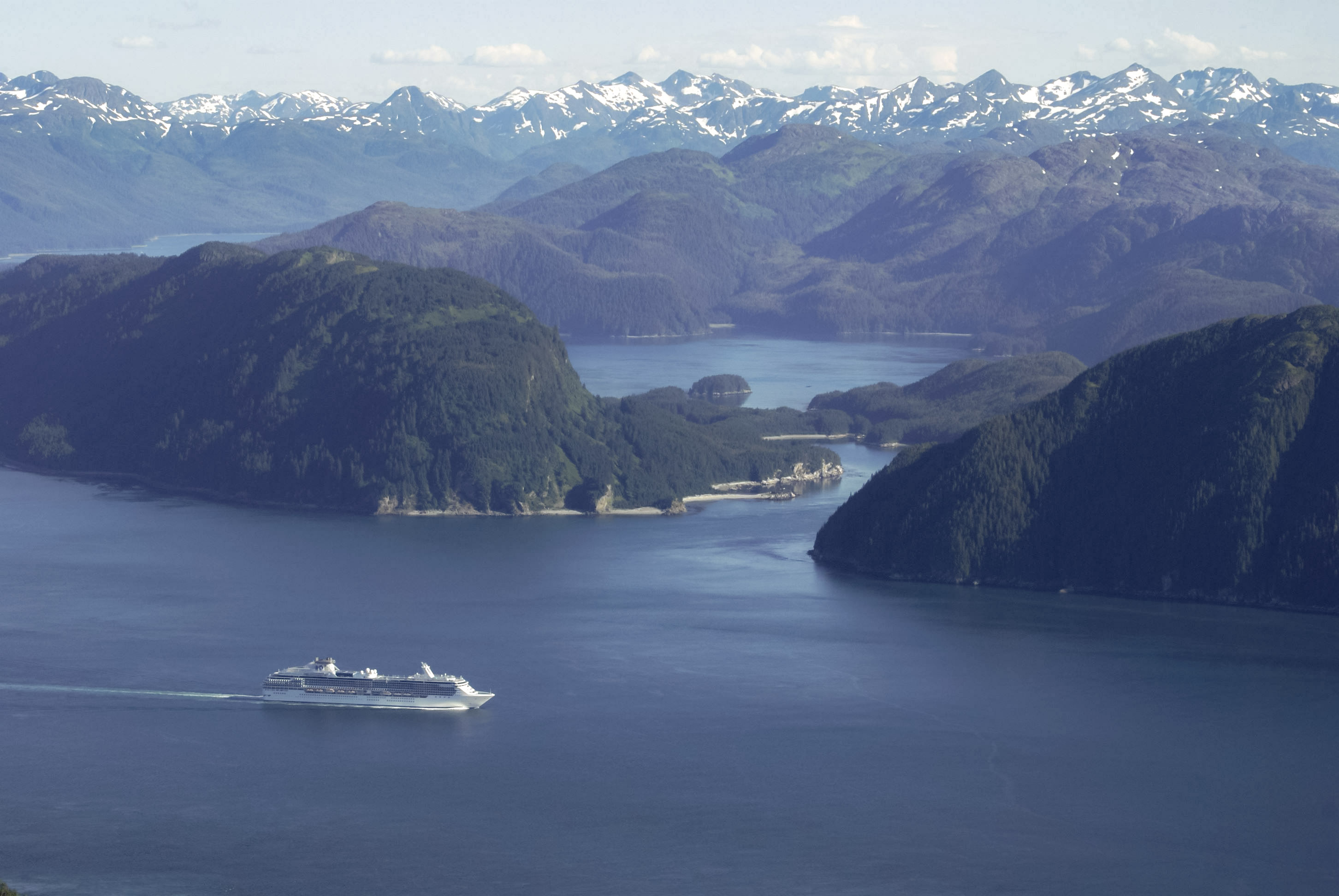 Aerial view of a white cruise ship boating through a large bay lined with mountains.