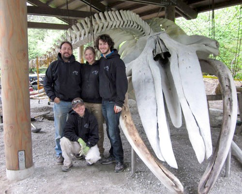 4 members of the whales and nails team poses beside the car-sized whale skull.