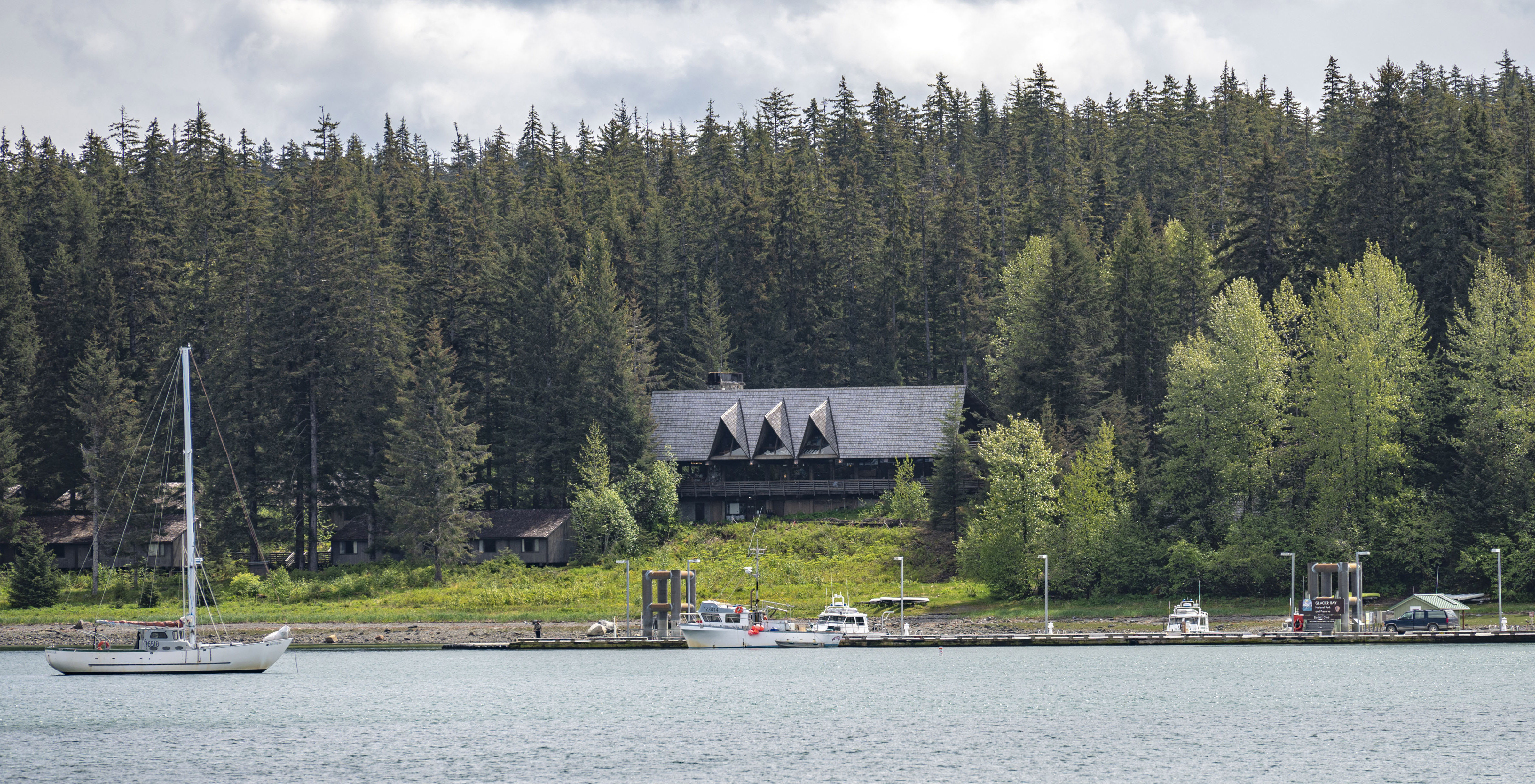 a view of the glacier bay lodge from the water, with the bartlett cove dock and a sailboat in the foreground.