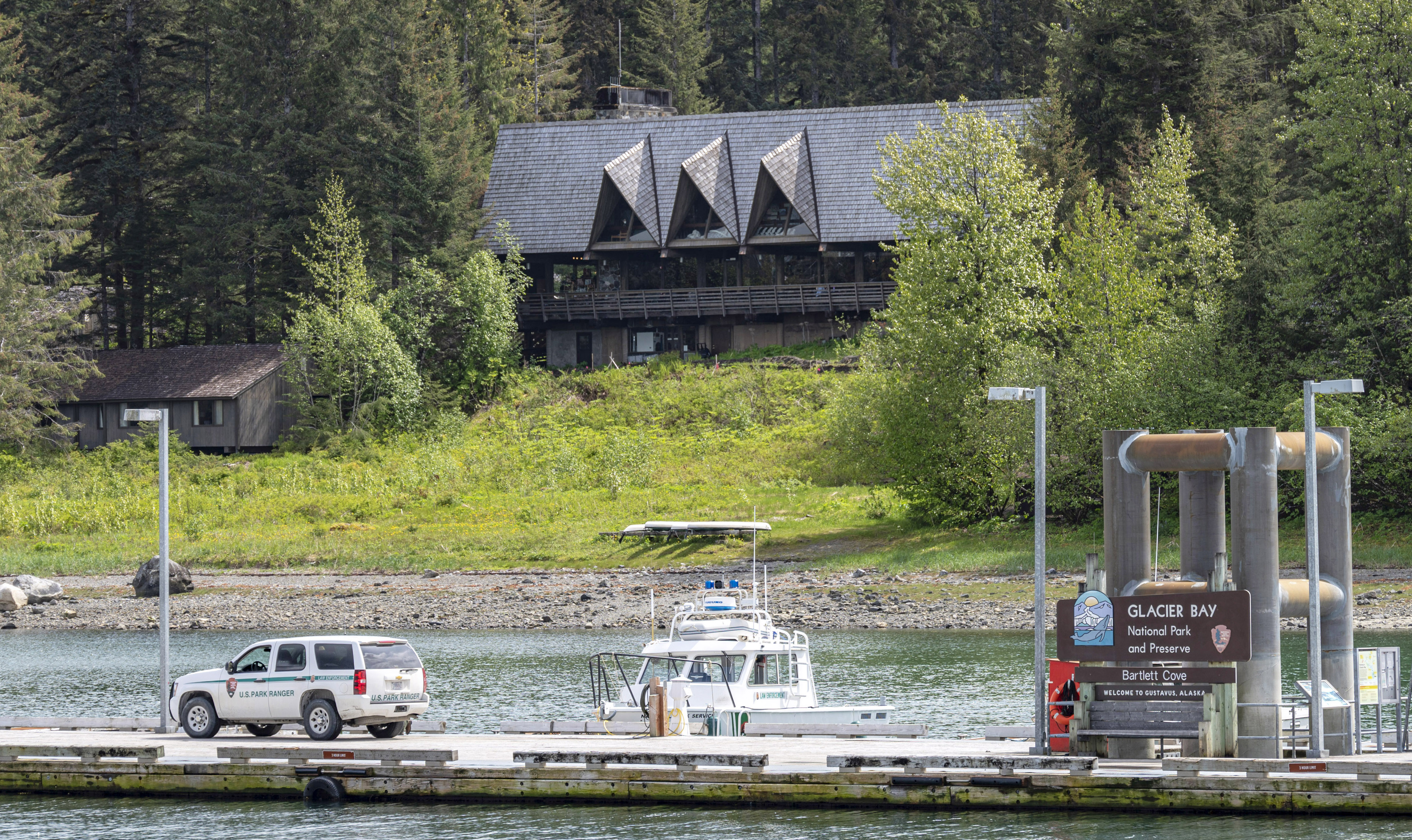 The Glacier Bay Lodge nestled in a dense forest on the shore of Bartlett Cove, the dock is visible in the foreground.