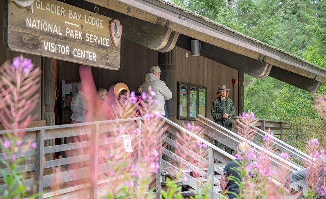 A park ranger stands on the porch of the Glacier Bay Lodge and Visitor Center and speaks with visitors.