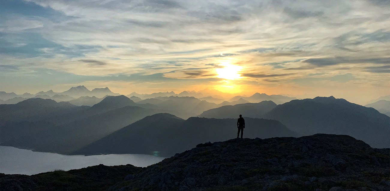 Person looks toward setting sun which casts shadows on countless mountains