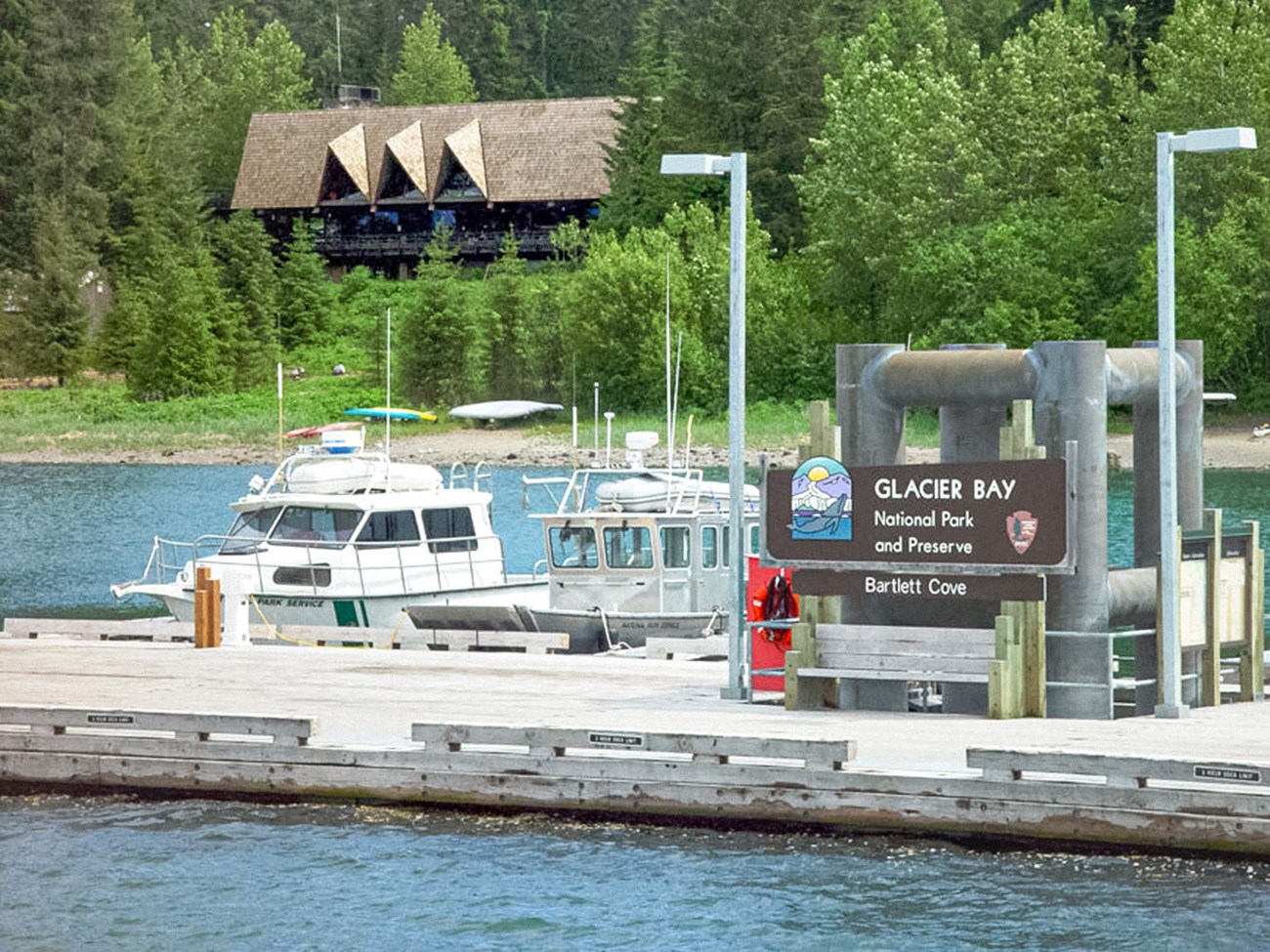 Glacier Bay welcome sign on the public dock with two NPS boats and Glacier Bay lodge in background on shore