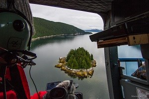 researcher looking out of helicopter at rocky shoreline gathering coastline imagry
