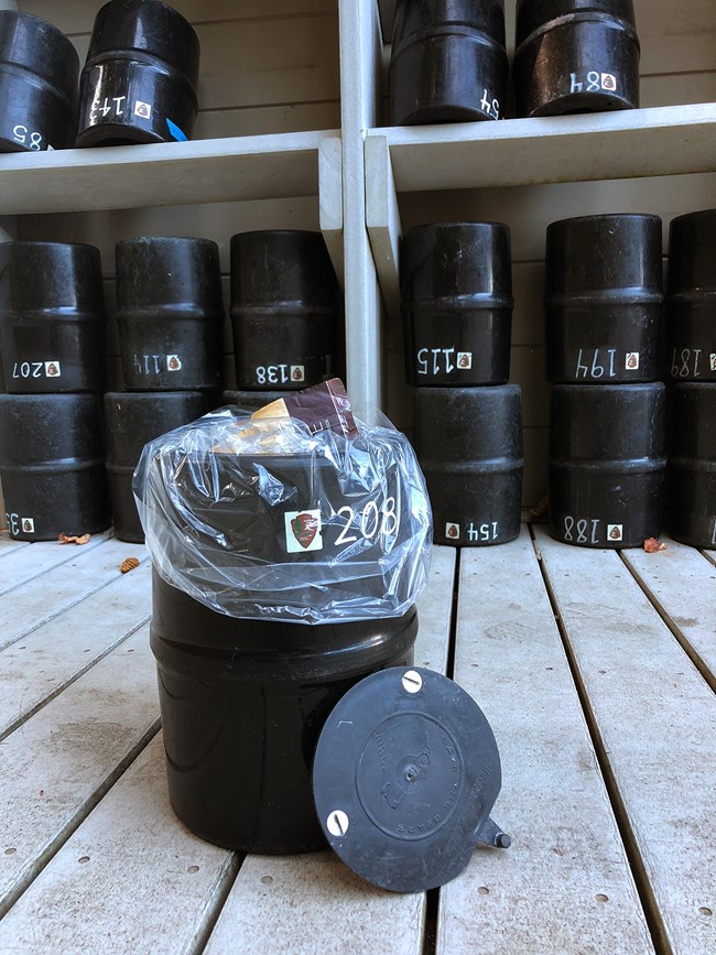 a black, cylindrical bear canister with a clear plastic liner and some food packets inside