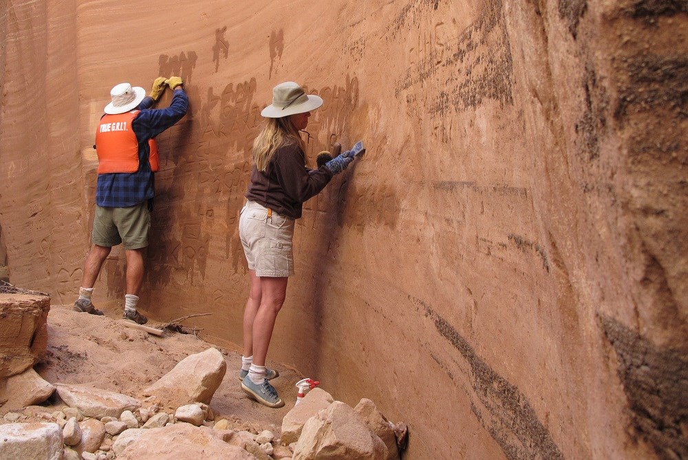 GRIT in canyon A man wearing a life jacket and a woman scrub a sandstone wall