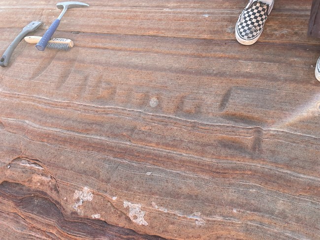 Graffiti carved into sandstone wall, with rock hammer and scrub-brush for scale