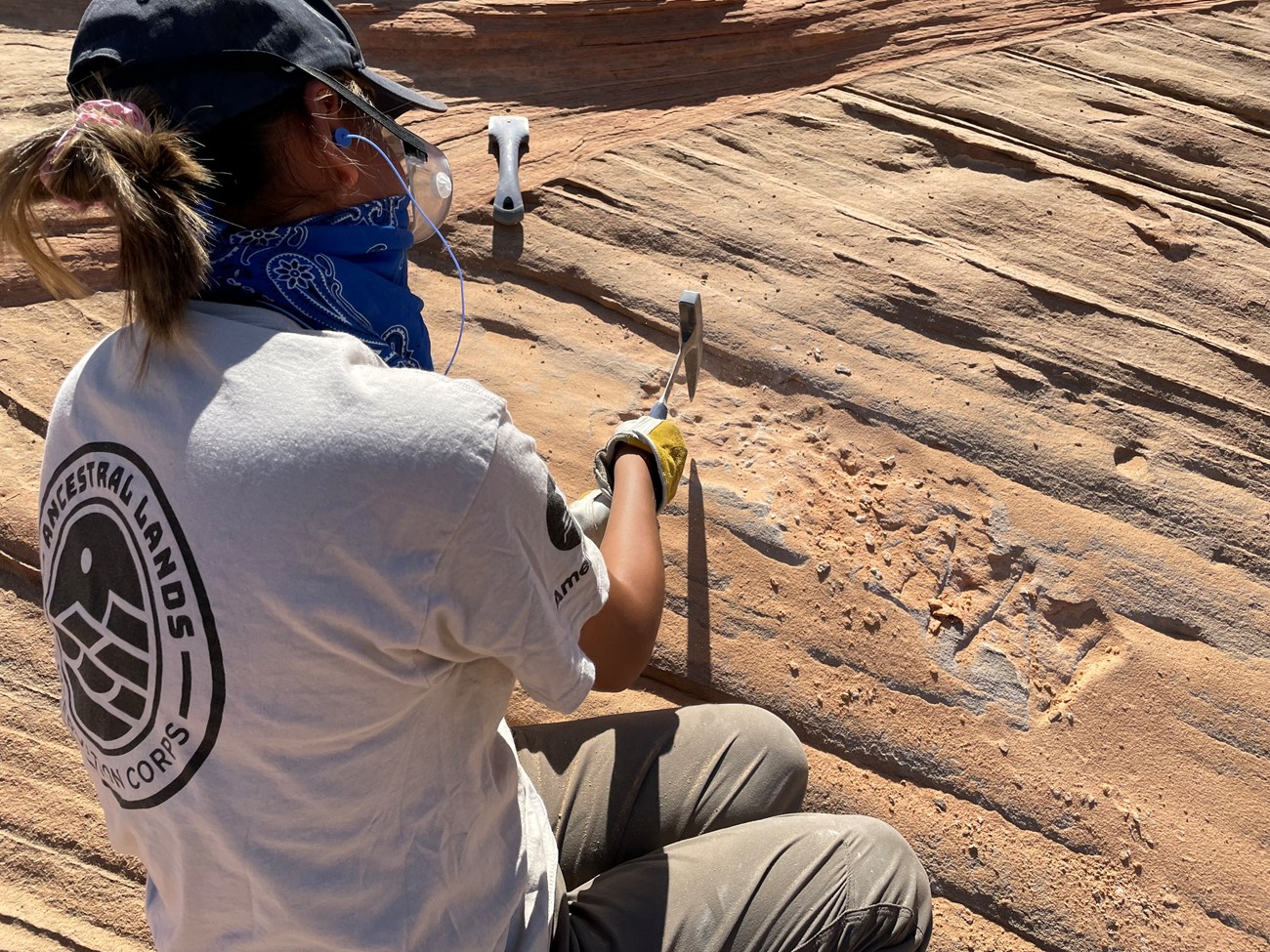 A person remove graffiti from sandstone with rock brush.