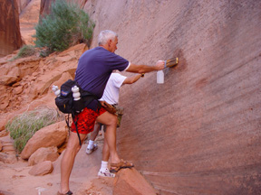 Two beople use squirt bottles and brushes to scrub graffiti off the canyon wall. Two beople use squirt bottles and brushes to scrub graffiti off the canyon wall.