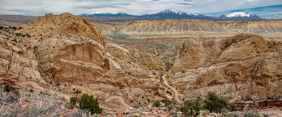 winding dirt road through sandy cliffs. Mountains in background.