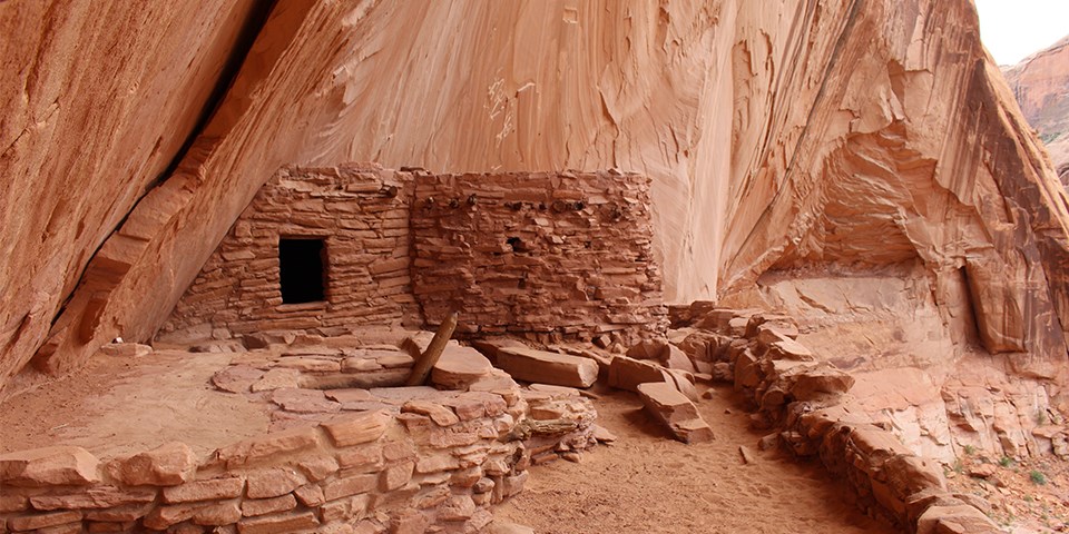 A circular dwelling made of layered sandstone nestled against canyon wall.