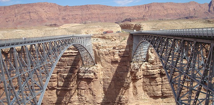 Two identical steel-arch bridges span across the canyon. A parking area on the other side. Two identical steel-arch bridges span across the canyon. A parking area on the other side.