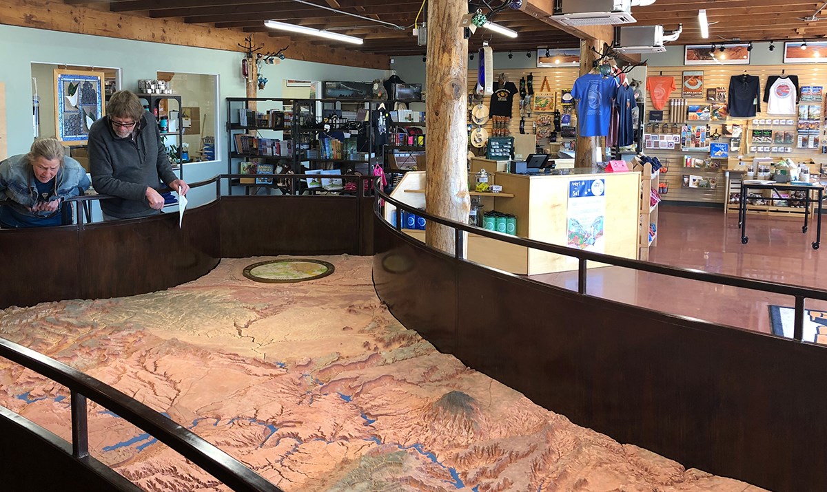 Visitors study a giant relief map inside a retail space with books and park merchandise