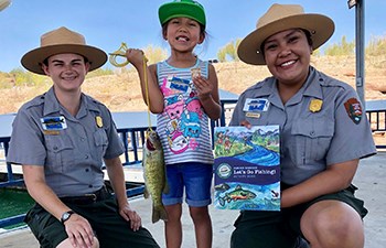 Rangers kneel by a young girl holding the fish she caught