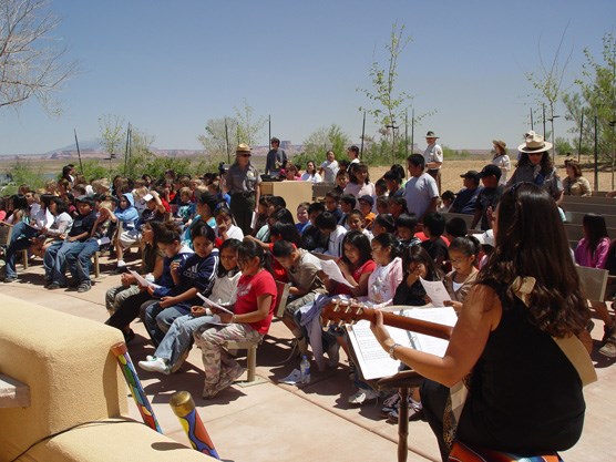 large group of kids, Park rangers, and a person playing guitar in open-air outdoor seating. large group of kids, Park rangers, and a person playing guitar in open-air outdoor seating.