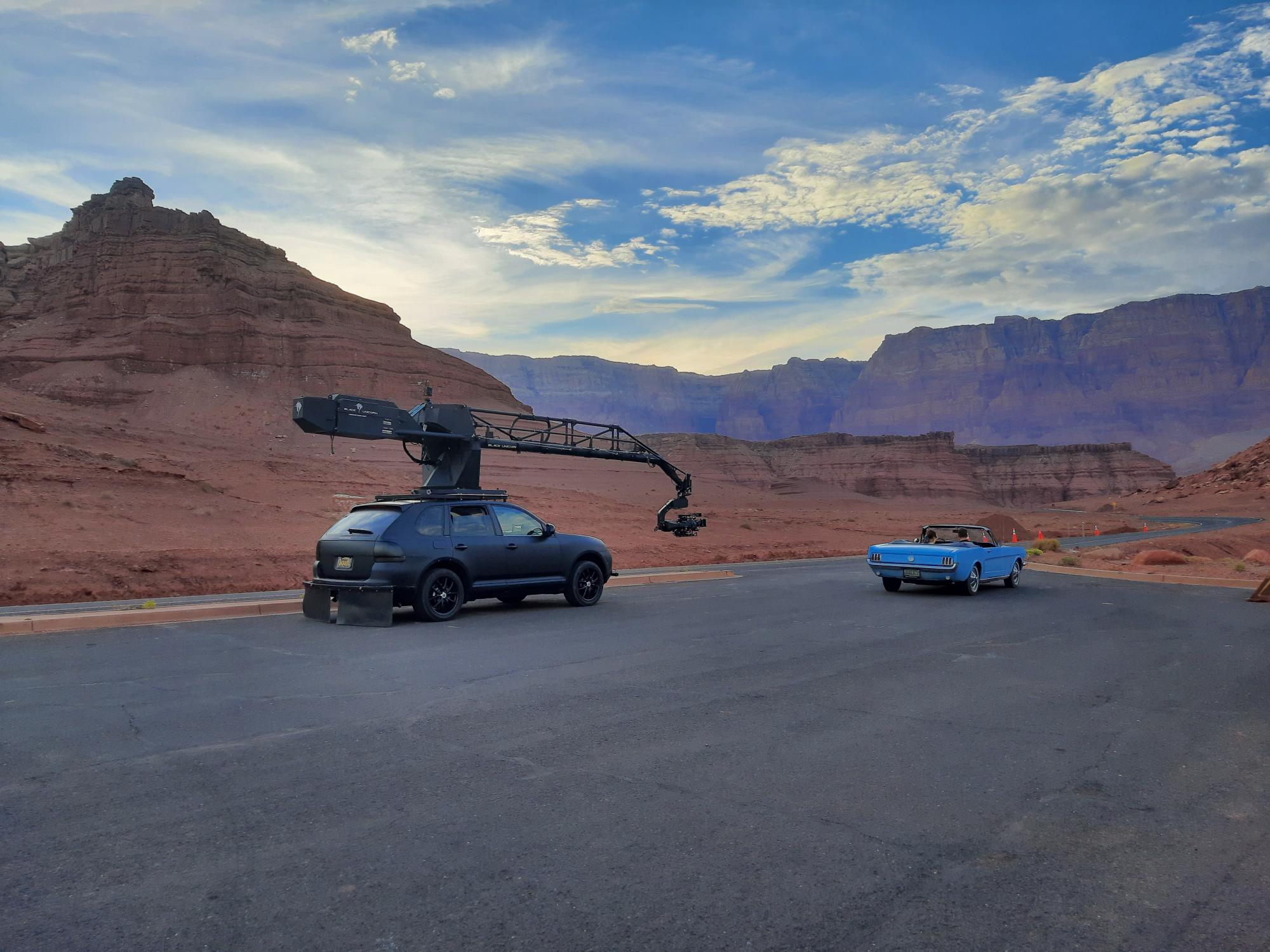 small SUV with large camera rigging equipment parked behind older sportscar in scenic red rock desert