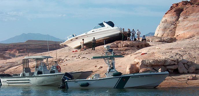 A white boat is stranded on the rocks high above the water. Park Rangers and Sheriffs and their boats surround the area. A white boat is stranded on the rocks high above the water. Park Rangers and Sheriffs and their boats surround the area.