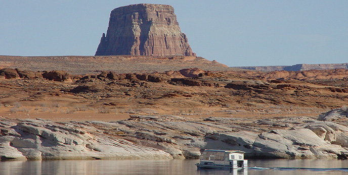 A large boat travels away from the camera towards a cliff wall. behind the cliff is a cylindrical butte. A large boat travels away from the camera towards a cliff wall. behind the cliff is a cylindrical butte.