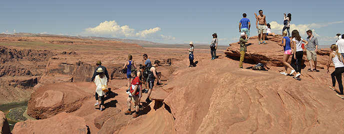 A large group of people stand on top of a sandstone rock. It's a long way down. A large group of people stand on top of a sandstone rock. It's a long way down.