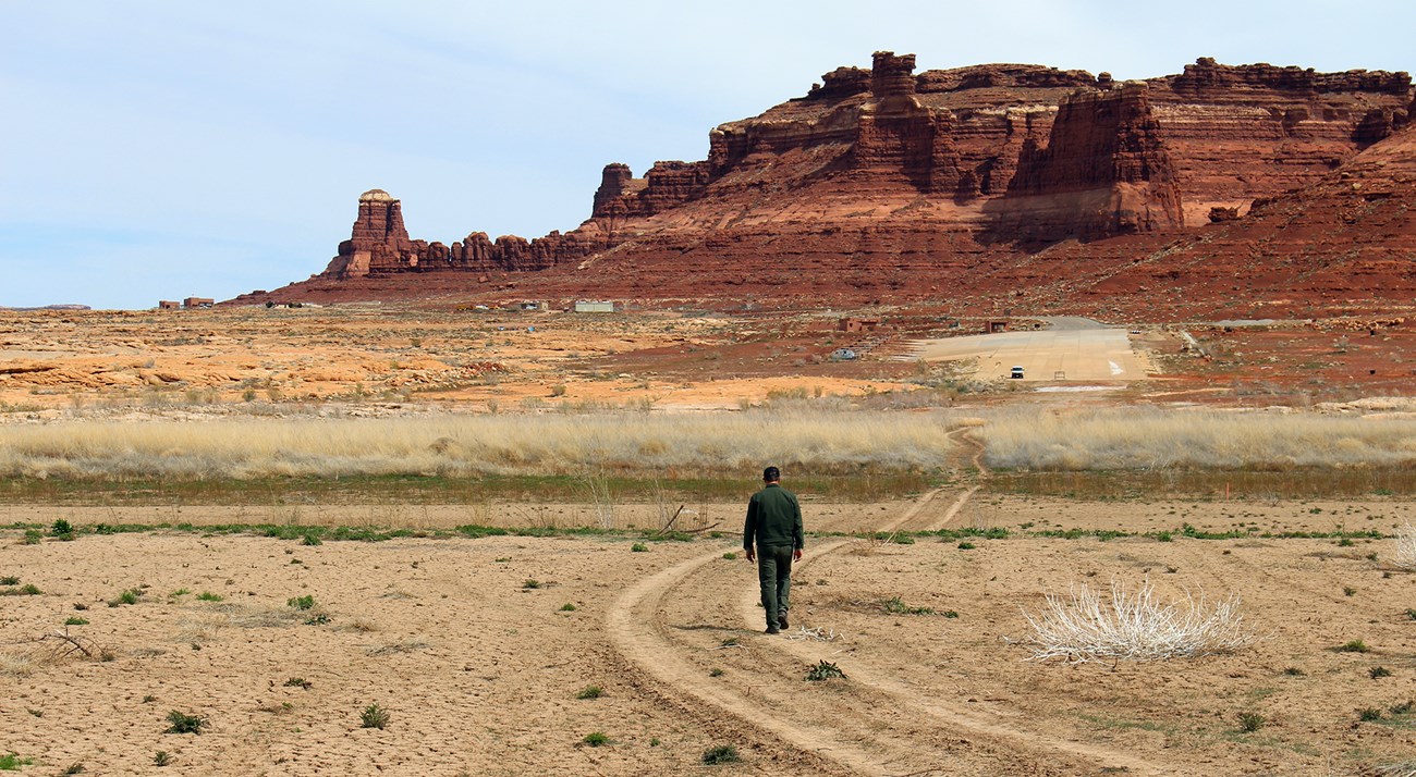 Ranger walks up dirt tracks toward paved launch ramp far away