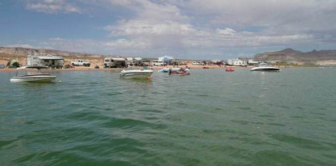 View from the water of a large group of boats near a sandy beach. The beach is full of campers, RVs, and tents. View from the water of a large group of boats near a sandy beach. The beach is full of campers, RVs, and tents.