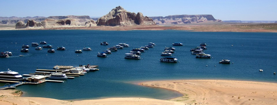 Beach, docks and houseboats on lake. Sandstone cliffs in background. Beach, docks and houseboats on lake. Sandstone cliffs in background.