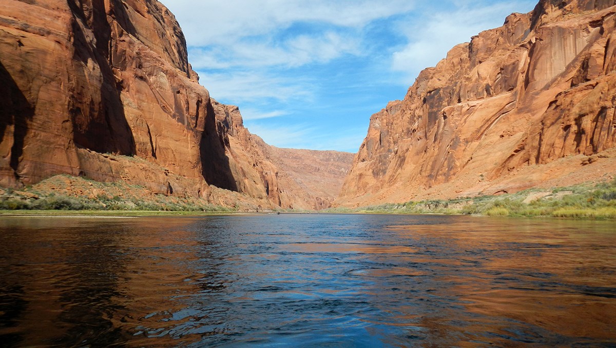 On a river between shoreline vegetation and sandstone canyon walls On a river between shoreline vegetation and sandstone canyon walls