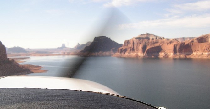The front of a seaplane from the inside of the cokpit. The propeller is a blur. Lake Powell and sandstone cliffs lie ahead. The front of a seaplane from the inside of the cokpit. The propeller is a blur. Lake Powell and sandstone cliffs lie ahead.