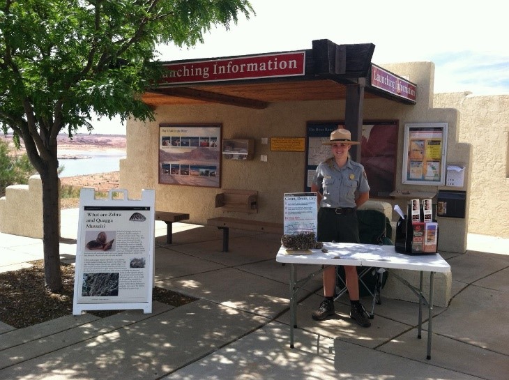 Park Ranger stands outdoors at table with information and flyers.