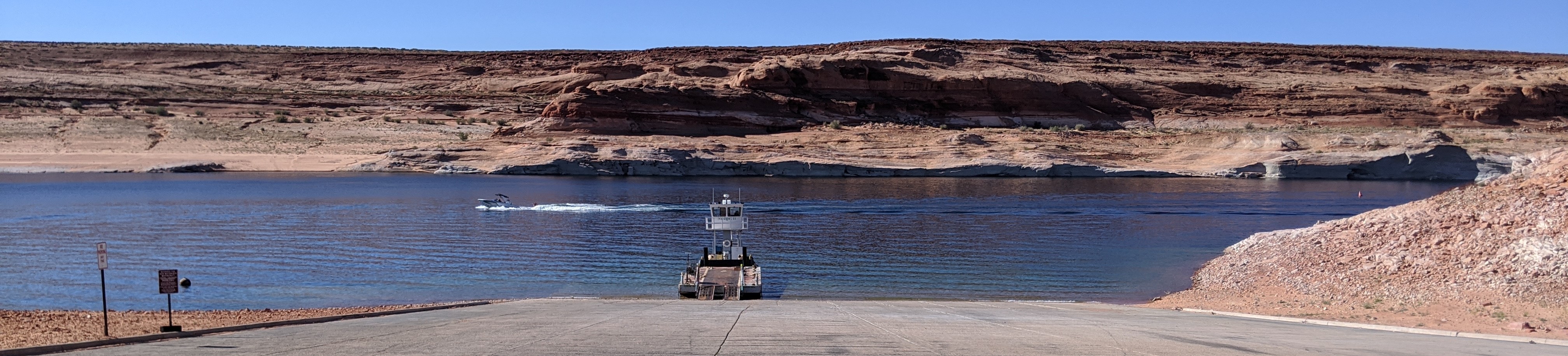 Large barge up against a concrete launch ramp on a desert lake in a sandstone canyon
