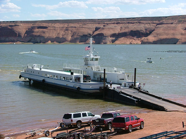 Large ferry boat docked. Cars with trailers parked on the beach nearby.