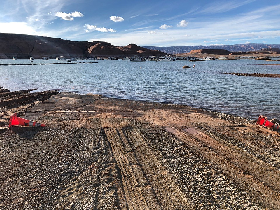 Gravel track leading to lake. Caution cones on the sides, sandstone cliffs in background.