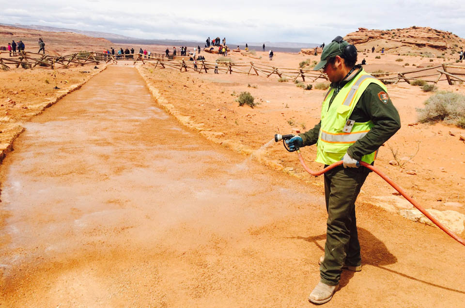 Worker with water hose on dirt trail