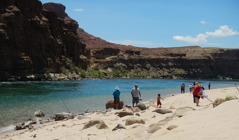 A river beach and a cliff, people fishing from shore.