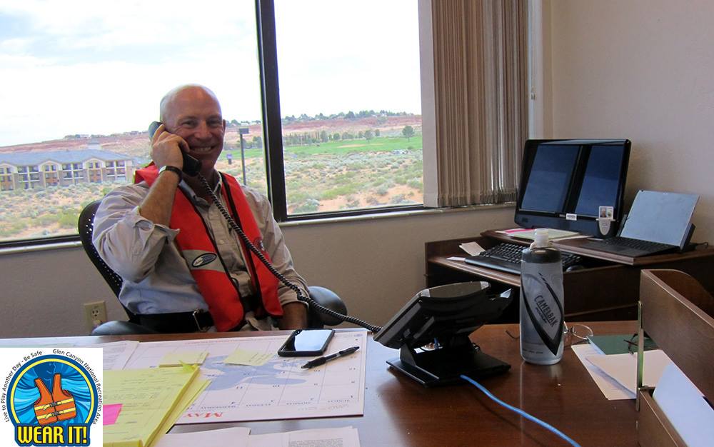 Wear Your Life Jacket to Work Day Man in business attire and a life jacket on phone at office desk