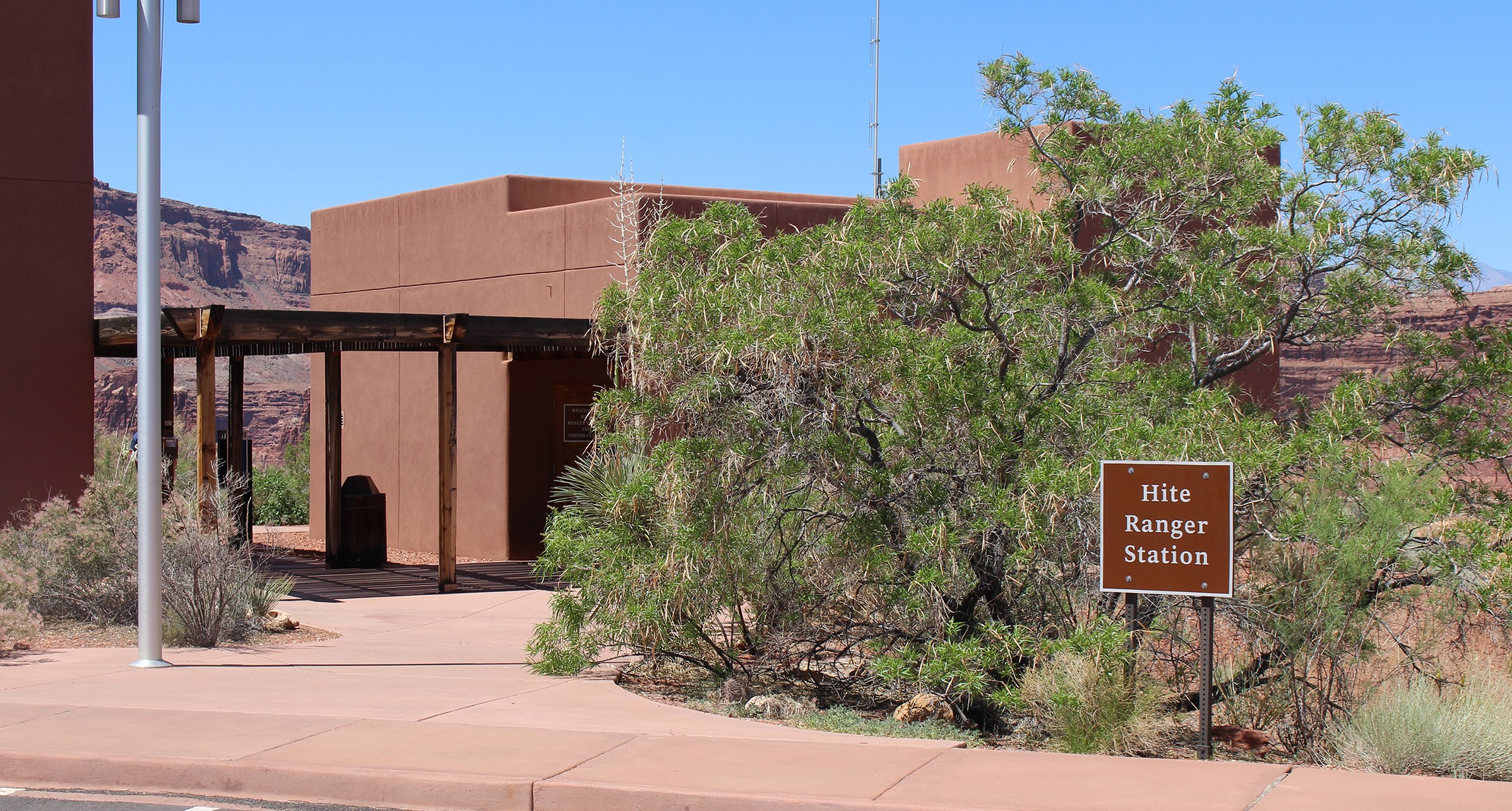 Hite RS (7a) Adobe building surrounded by scrubby trees. Sign says Hite Ranger Station.