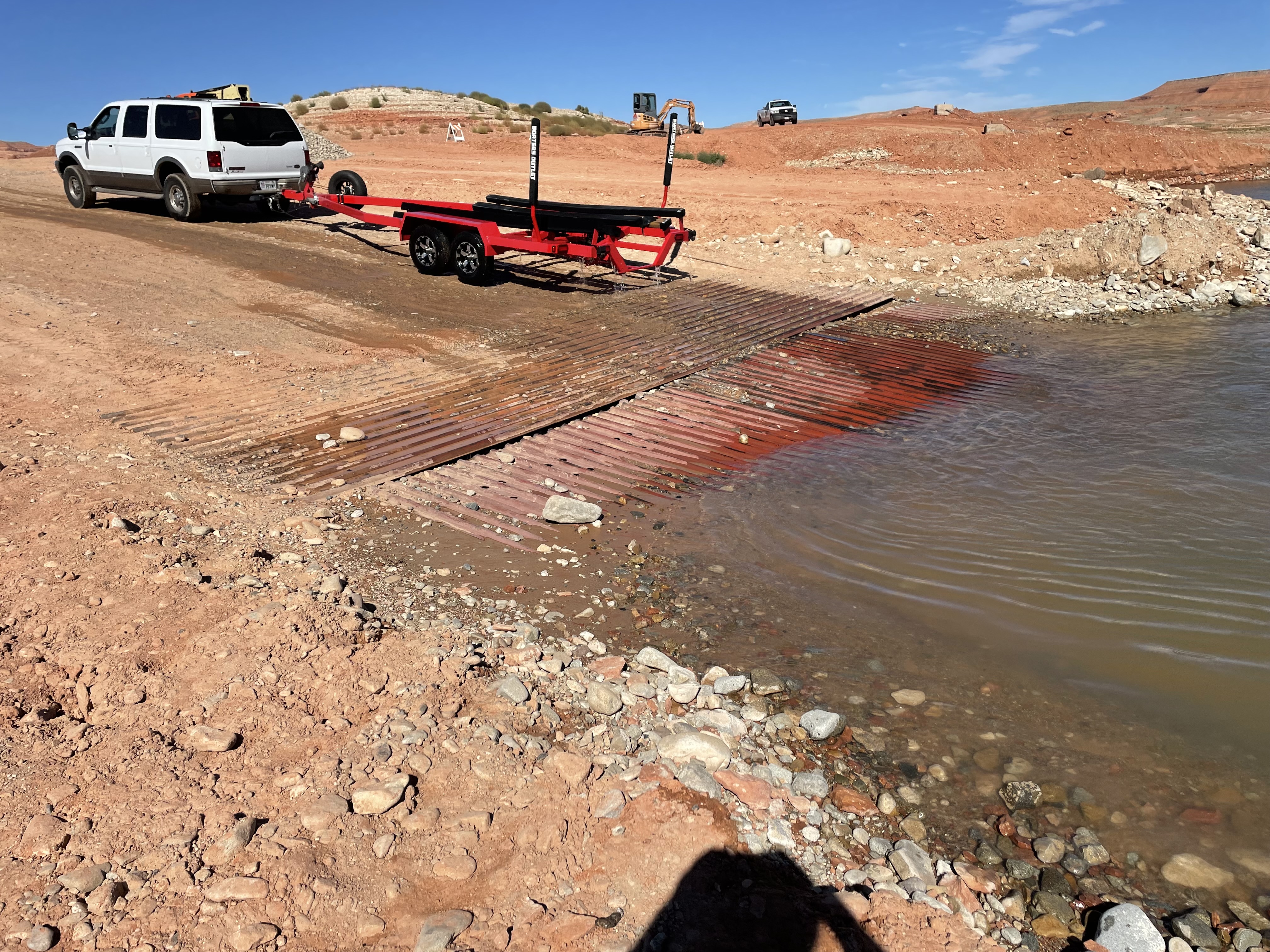 Back end of boat on a trailer on dirt and metal pipe road at water's edge