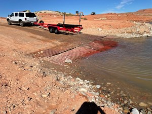 Back end of boat on a trailer on dirt and metal pipe road at water's edge