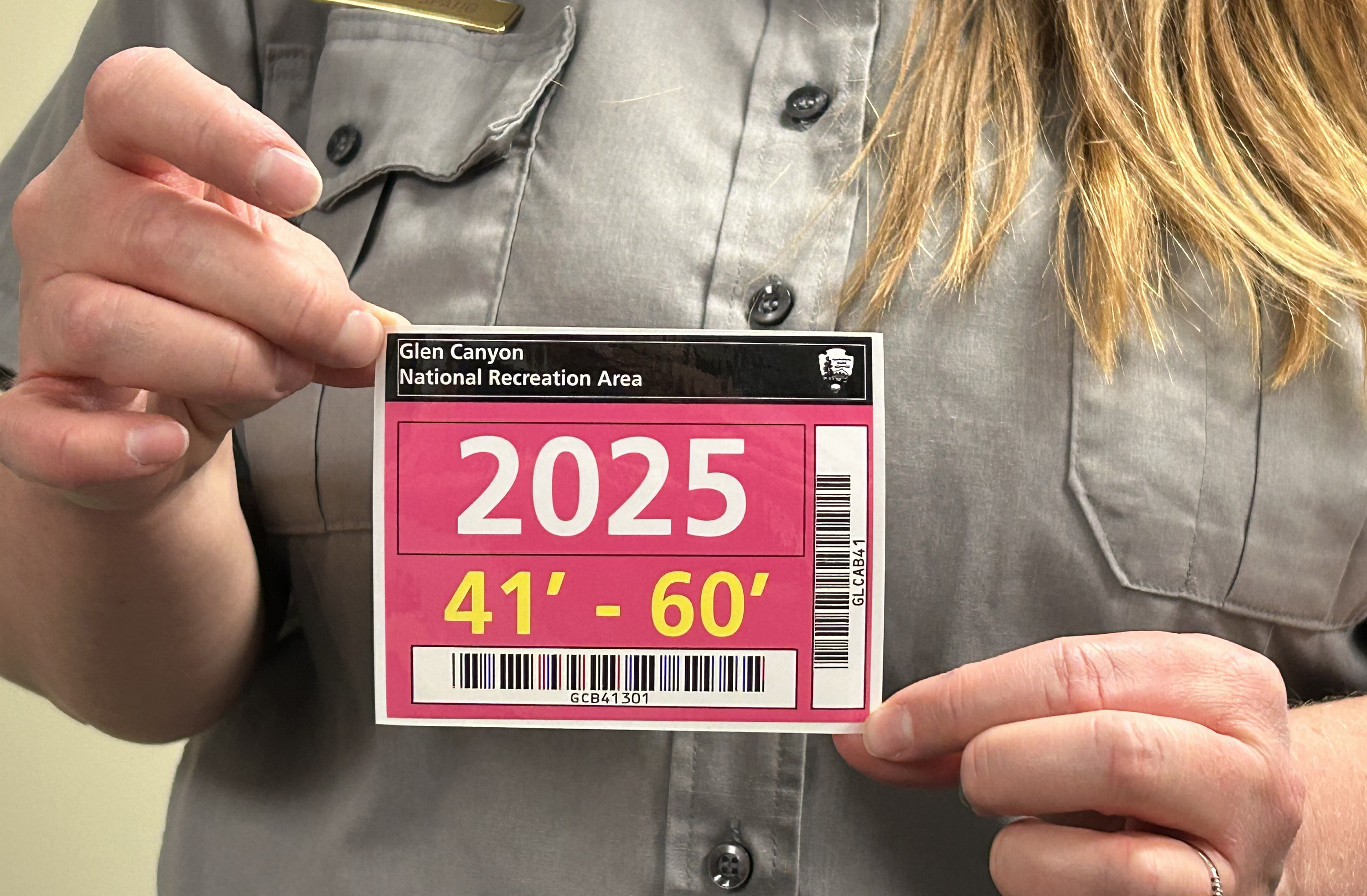 GLCA 2025 tiered vessel pass Park ranger holding a decal pass close to the chest. The pass is bright pink with a black top and "2025" written on it.