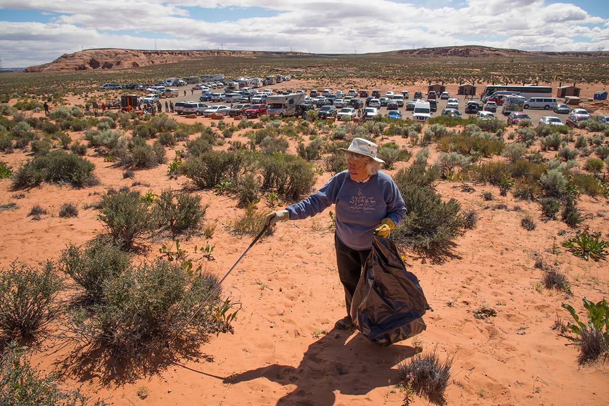 Woman uses grippers to pick up litter from hill above busy parking lot