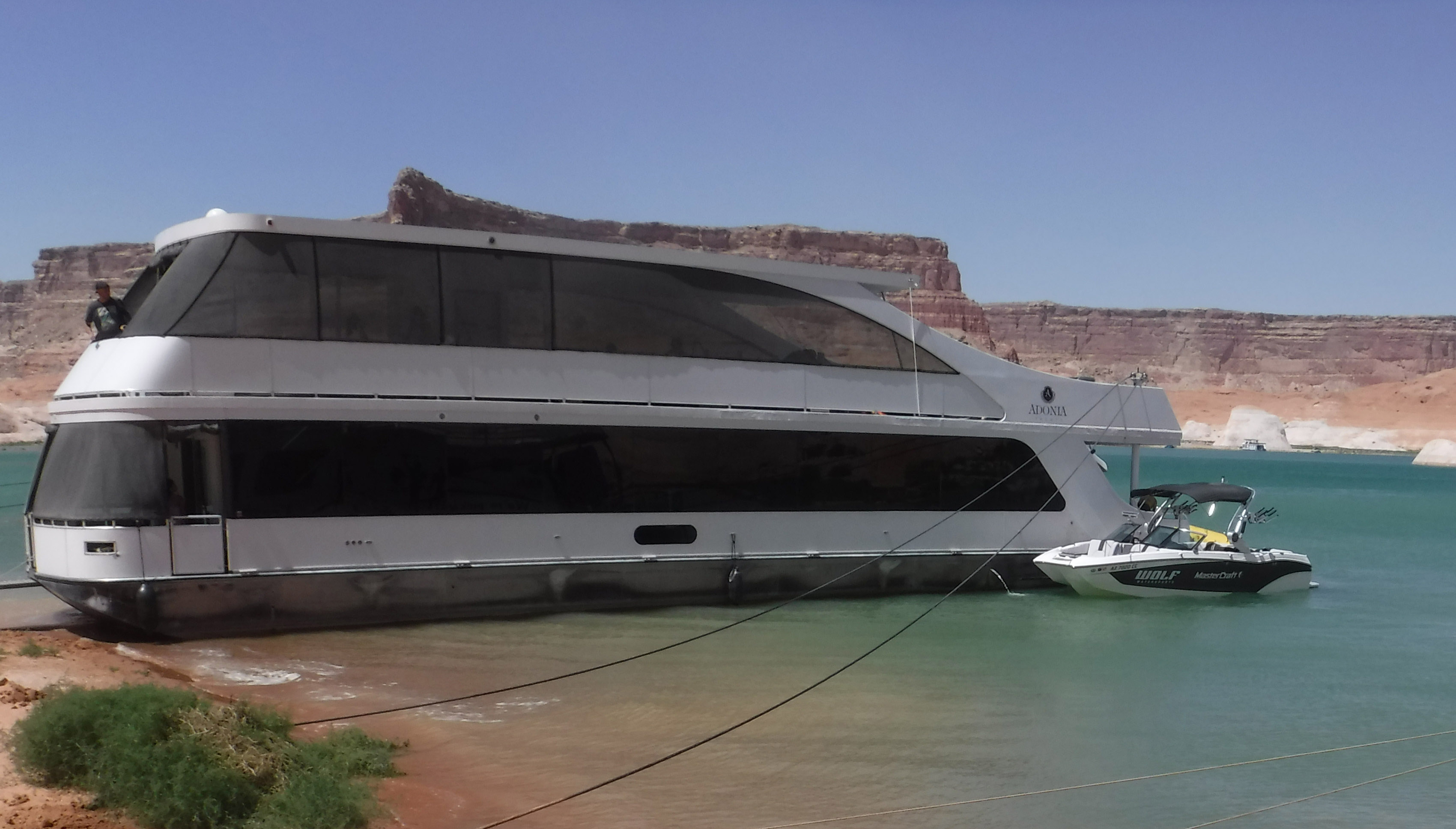 Boats on Lake Powell A large, two story houseboat beached next to a small motor boat on a lake.