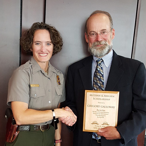 A female ranger and bearded man stand holding a wooden plaque