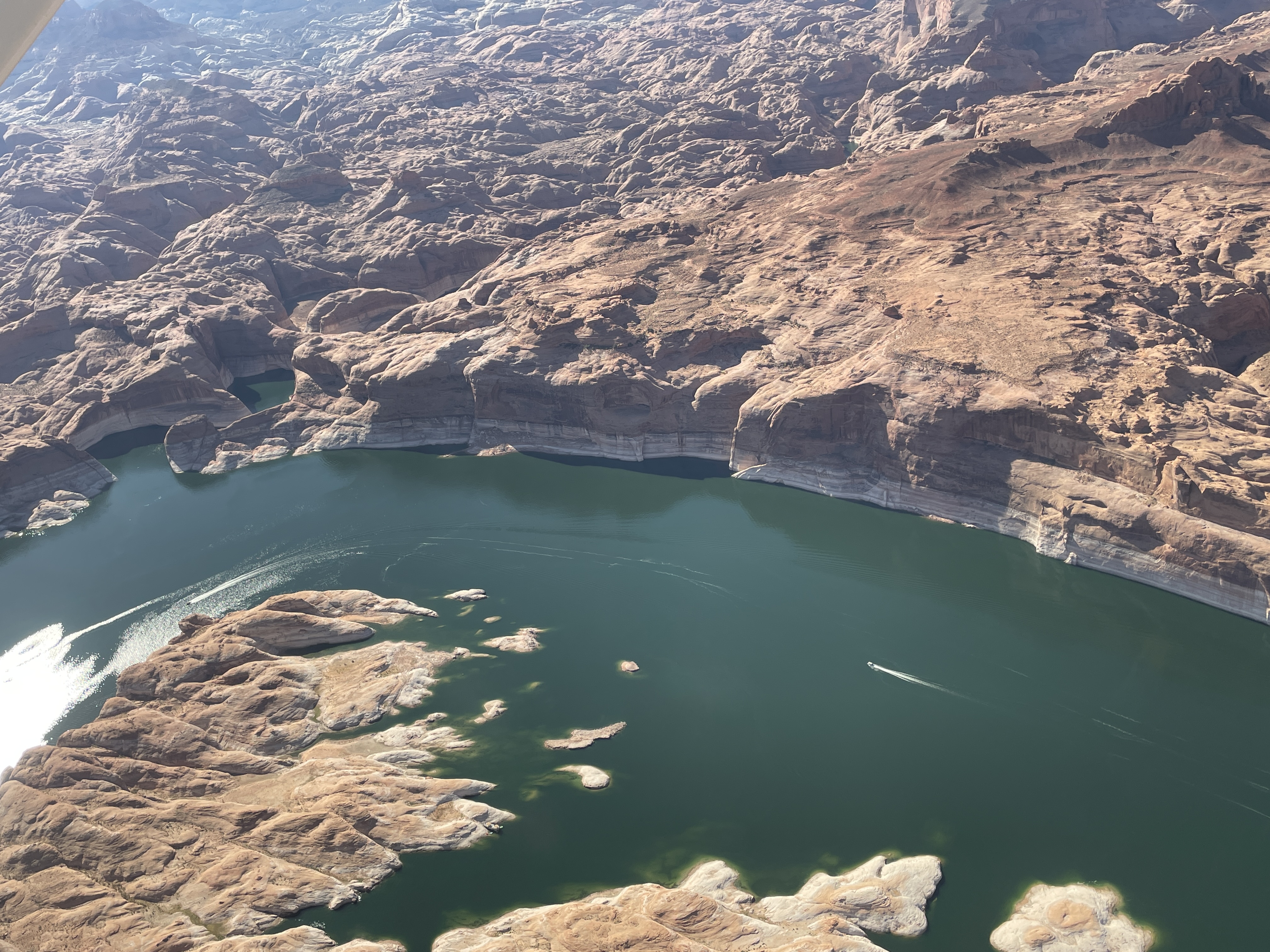 Aerial view of a desert lake surrounded by sandstone cliffs. Housboatts scattered on the lake.