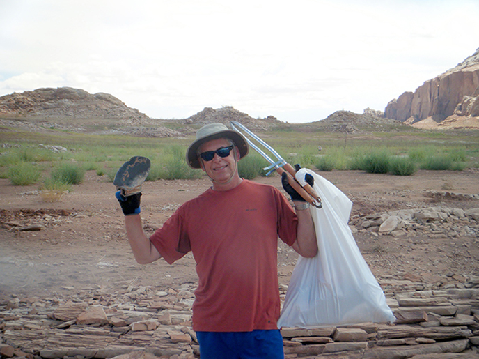 A man in a hat holds up a trash bag and grabbers.