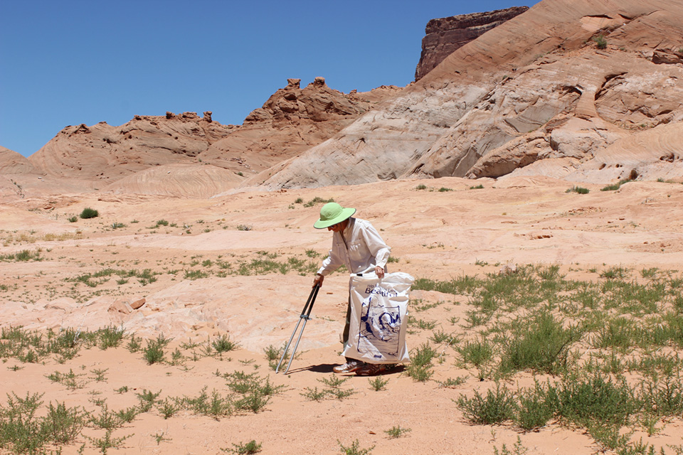 Woman in wide hat removes litter from sand