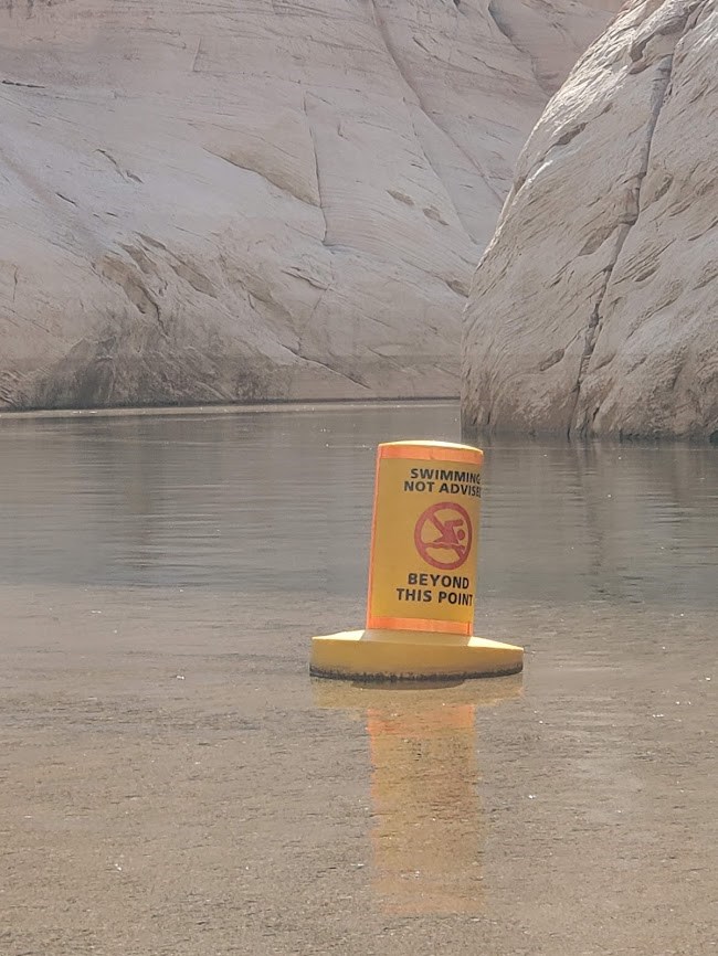 Yellow buoy with orange trim and words: Swimming not advised beyond this point" in murky water.