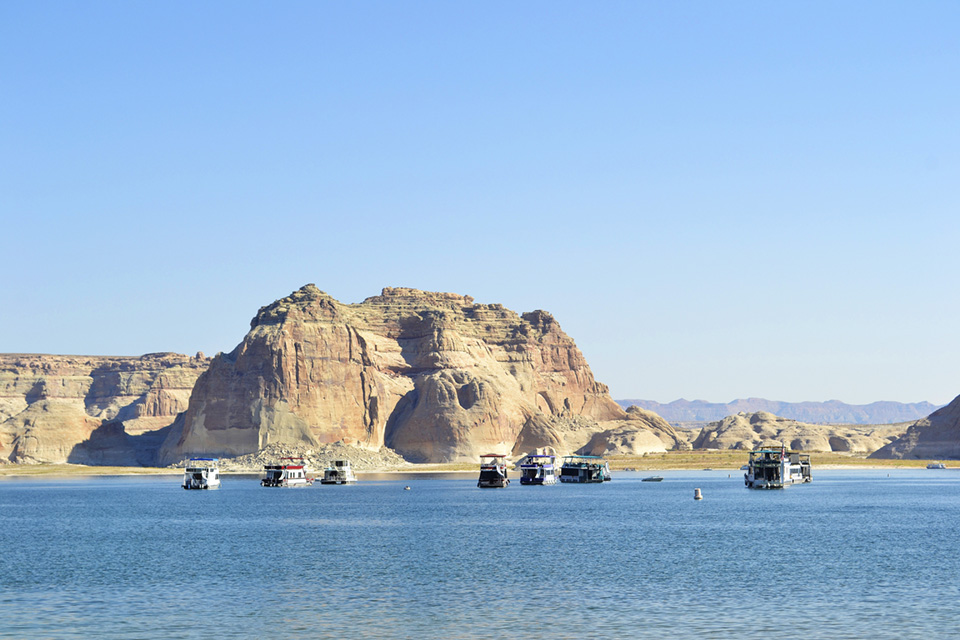 lake with large sandstone walls behind, houseboats near beach